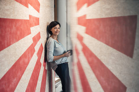 Female entrepreneur with coffee cup in office against wall stock photo