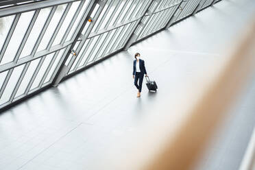 Businesswoman with suitcase walking in corridor during pandemic - JOSEF03683