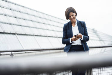 Smiling businesswoman text messaging on mobile phone outside office building - JOSEF03690