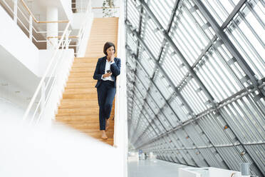 Unternehmerin mit Smartphone auf einer Treppe im Flur stehend - JOSEF03706