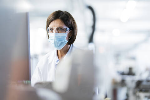 Technikerin mit Schutzbrille im Labor während COVID-19, lizenzfreies Stockfoto