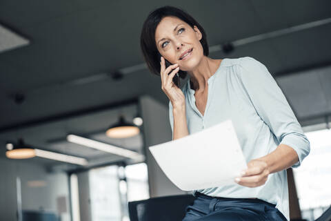 Female entrepreneur with document talking on smart phone at office stock photo