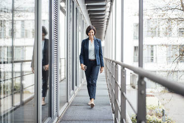 Smiling female entrepreneur walking in office balcony - JOSEF03723