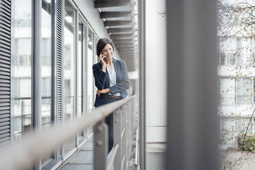 Female professional talking on mobile phone while standing in office balcony - JOSEF03728