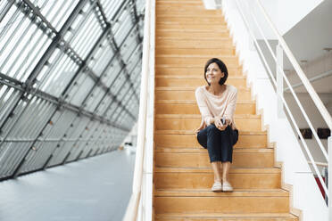Nachdenkliche Geschäftsfrau, die auf einer Treppe im Korridor sitzt - JOSEF03730