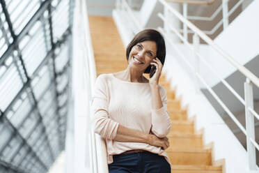 Smiling female entrepreneur talking on smart phone against steps - JOSEF03734