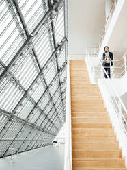 Weibliche Fachkraft steht an einem Geländer über einer Treppe im Büro - JOSEF03735