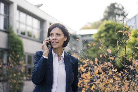 Mature businesswoman talking on smart phone at office park stock photo