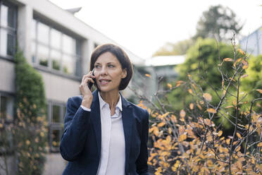 Mature businesswoman talking on smart phone at office park - JOSEF03736