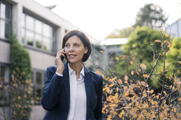 Reife Geschäftsfrau, die im Büropark mit ihrem Smartphone telefoniert - JOSEF03736