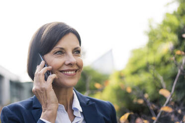 Smiling female entrepreneur talking on mobile phone at office park - JOSEF03737