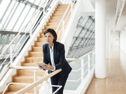 Selbstbewusste Geschäftsfrau mit digitalem Tablet, die sich am Geländer eines Korridors anlehnt - JOSEF03738