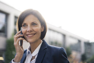 Happy businesswoman talking on mobile phone at office park - JOSEF03740