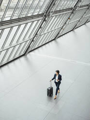 Mature businesswoman with suitcase walking at corridor - JOSEF03742