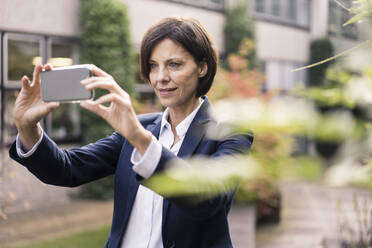 Geschäftsfrau, die ein Selfie macht, während sie im Büropark steht - JOSEF03745