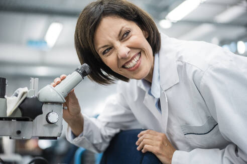 Smiling female scientist holding microscope at laboratory - JOSEF03755