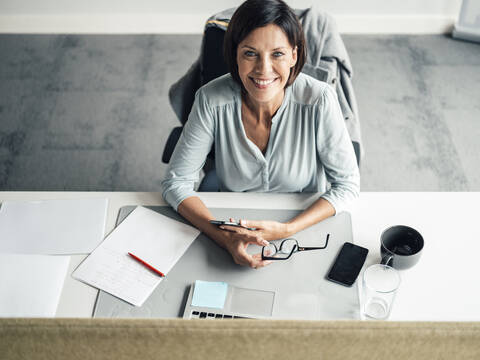 Smiling female entrepreneur sitting on chair at desk in office stock photo