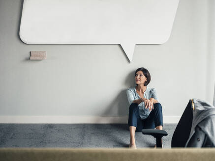 Thoughtful businesswoman looking up while sitting on floor at office - JOSEF03761