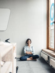 Businesswoman with arms crossed sitting on floor at office against wall - JOSEF03764