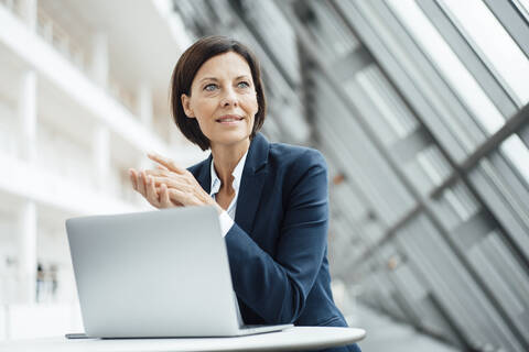 Weibliche Fachkraft mit Laptop, die im Büro wegschaut, lizenzfreies Stockfoto