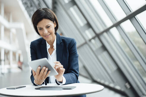 Smiling businesswoman using digital tablet at desk in corridor - JOSEF03779