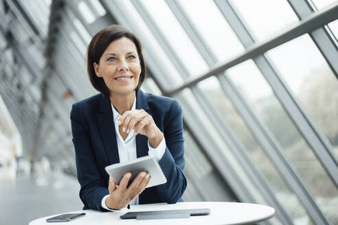 Businesswoman holding digital tablet at desk in corridor - JOSEF03780