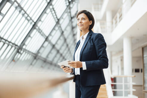 Mature businesswoman with digital tablet in corridor at office - JOSEF03781