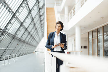 Businesswoman with digital tablet contemplating at corridor - JOSEF03784