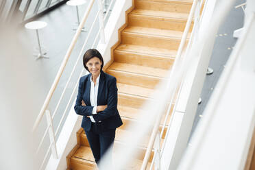 Confident businesswoman with arms crossed standing on steps in corridor - JOSEF03787