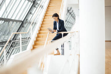 Businesswoman using digital tablet while leaning on railing in corridor - JOSEF03789