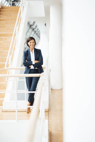 Female entrepreneur with arms crossed by railing in corridor stock photo