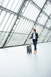 Female entrepreneur with suitcase looking away while walking in corridor - JOSEF03794