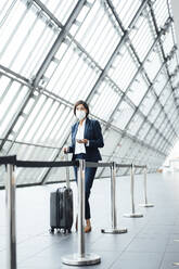 Businesswoman with suitcase standing in corridor during pandemic - JOSEF03796