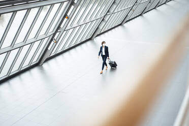 Businesswoman with suit case walking in corridor during COVID-19 - JOSEF03797