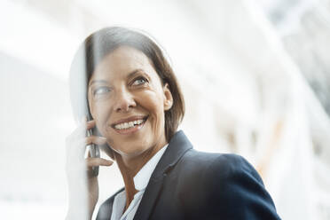 Lächelnde Geschäftsfrau, die im Büro mit einem Mobiltelefon spricht - JOSEF03805