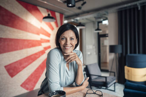 Smiling businesswoman leaning on table at office - JOSEF03816