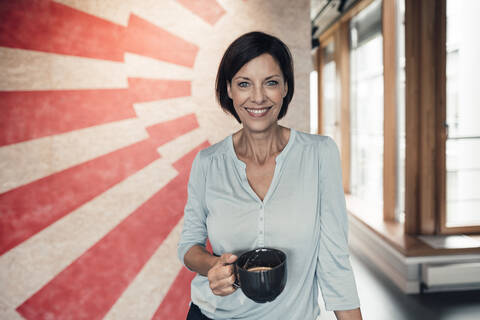 Confident female entrepreneur with coffee cup in office stock photo