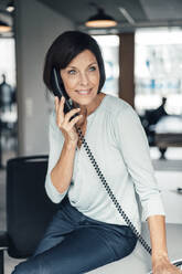 Mature businesswoman talking through telephone in office - JOSEF03822
