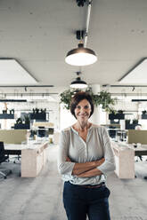 Female professional with arms crossed standing at illuminated office - JOSEF03827