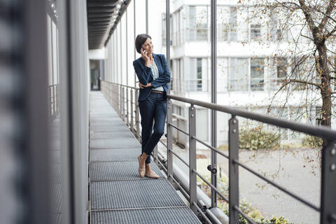 Businesswoman talking on mobile phone while standing on balcony at office stock photo