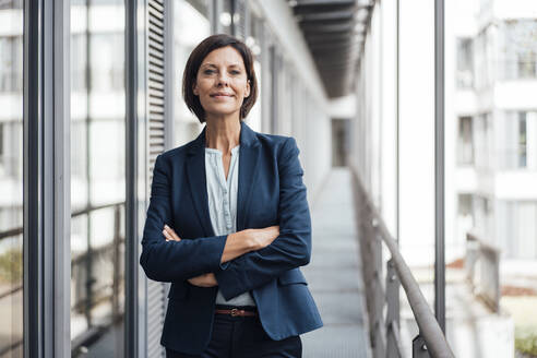 Smiling confident businesswoman with arms crossed standing on balcony - JOSEF03833
