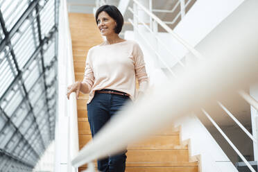 Businesswoman looking away while standing on steps on corridor - JOSEF03843