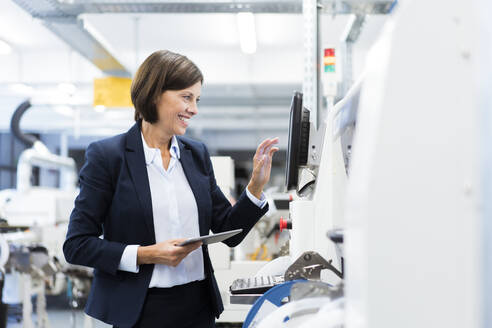Happy businesswoman with digital tablet operating machinery in factory - JOSEF03855