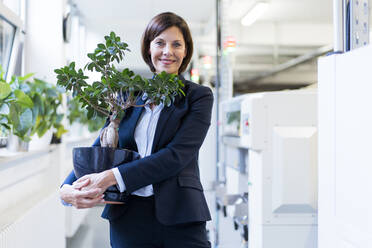 Lächelnde Geschäftsfrau mit Topfpflanze in der Industrie - JOSEF03858