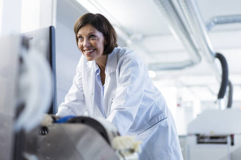 Smiling female scientist examining machinery at laboratory - JOSEF03865