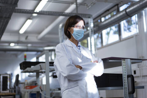 Wissenschaftlerin mit verschränkten Armen im Labor während einer Pandemie, lizenzfreies Stockfoto