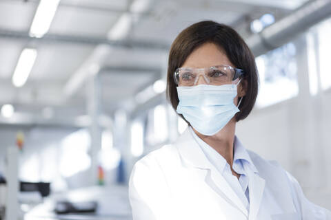 Mature female technician looking away in factory during pandemic stock photo