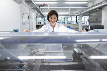 Smiling female technician by machinery in industry - JOSEF03882