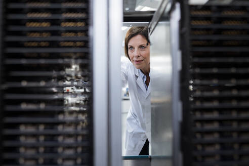 Mature female technician examining machinery at factory - JOSEF03884