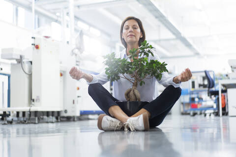 Female entrepreneur meditating while sitting on floor in industry stock photo